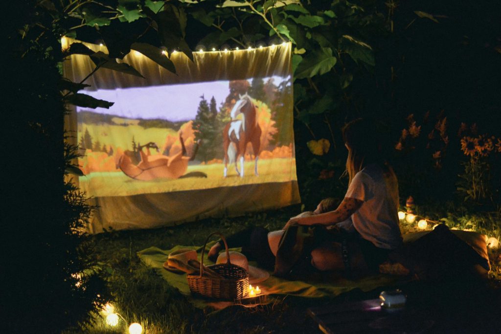 Couple enjoying a backyard movie night with a projector screen and picnic blanket setup