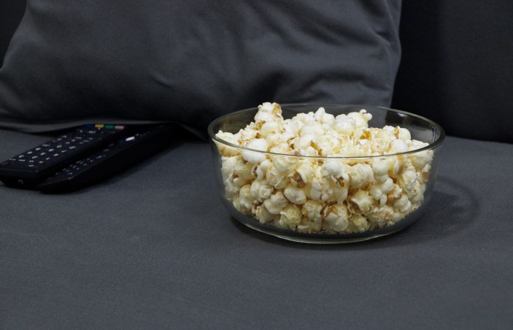 Bowl of popcorn and TV remotes on a sofa set up for a movie marathon