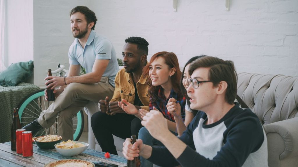 Group of friends watching a sports game on TV at a watch party with snacks