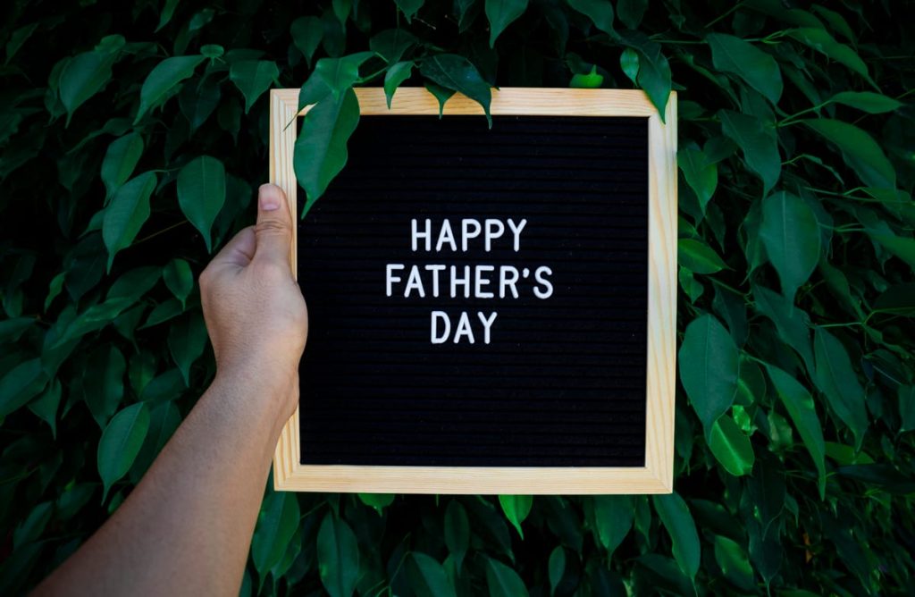 Hand holding a Happy Father's Day letter board sign against green leaves